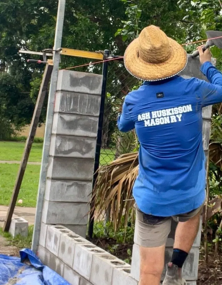 A bricklayer in a blue work shirt building a block pier